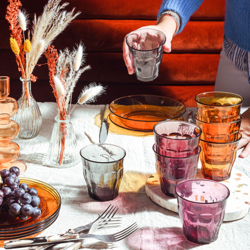 Verres Picardie de Duralex couleur ambre, prune et gris sur une table dressée avec une nappe blanche