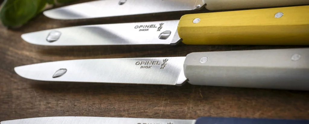Couteaux de table Opinel à manches colorés posés sur une table en bois