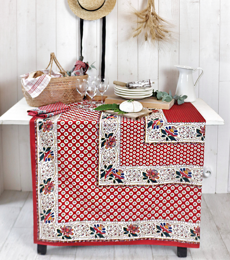 Nappe Souleiado rouge à motifs provençaux et bordure fleurie sur une table avec des verres et un pichet blanc